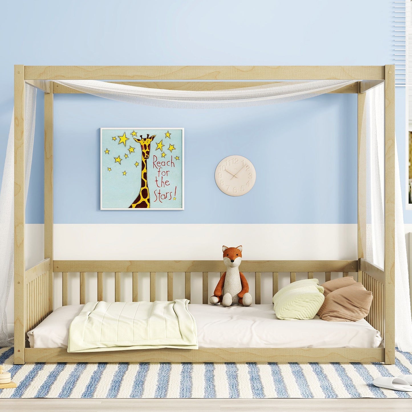 A child's room features a Canopy Frame Floor Bed with wooden guardrails, draped in white fabric, and decorated with a toy fox and pillows. Beneath is a blue and white striped rug. The wall displays giraffe artwork stating "Reach for the Stars!" alongside a round clock.