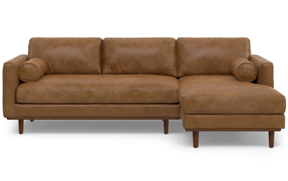 The Morrison Mid Century Sectional in Genuine Leather is a brown leather sectional sofa with a minimalist design. It includes three seat cushions and an extended chaise on the right side, complete with round bolster pillows at both ends, and rests on short wooden legs.