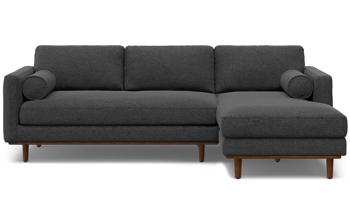 Introducing the Morrison Mid Century Sectional in Genuine Leather: a dark gray sofa with three seat cushions, three back cushions, and a chaise on the right side. It features cylindrical bolster pillows and wooden legs, embodying a modern and minimalist design.