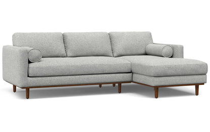 The Morrison Mid Century Sectional in Genuine Leather is a contemporary gray sofa with wooden legs and a right-side chaise lounge. It includes three back cushions and two cylindrical side cushions for a stylish and comfortable seating arrangement.