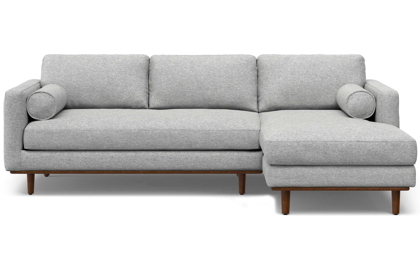 The Morrison Mid Century Sectional in Genuine Leather is a modern gray sectional sofa with wooden legs, featuring three back cushions and an extended chaise on the right. Two round bolster pillows are placed on the arms of the sofa.