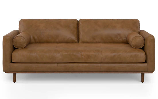 The Morrison 89-Inch Sofa and Ottoman Set in Genuine Leather showcases a modern design with its brown leather upholstery. It includes two seat cushions, two back cushions, and features two cylindrical bolster pillows on the arms. The sofa elegantly stands on wooden legs.