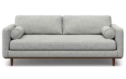 The Morrison 89-Inch Sofa and Ottoman Set in Genuine Leather features a modern, light gray design with two large back cushions, round bolster pillows on each side, and wooden legs for a minimalistic and clean aesthetic.