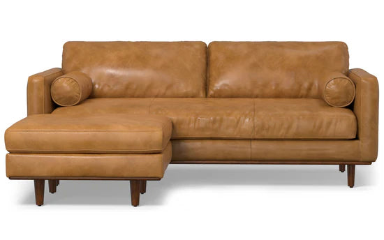 The Morrison 89-Inch Sofa and Ottoman Set in Genuine Leather is a tan leather sectional with clean lines and a modern design. It includes a left-side chaise, two round bolster pillows, and wooden legs that enhance its contemporary style.