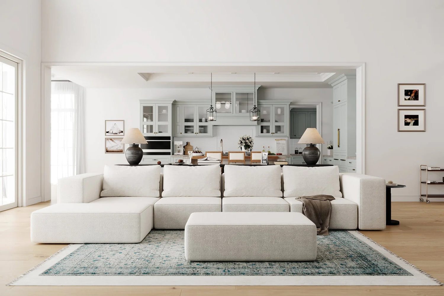 Blocky white sectional sofa with wide arms and an ottoman in a large, bright living room. In the background is a kitchen. 