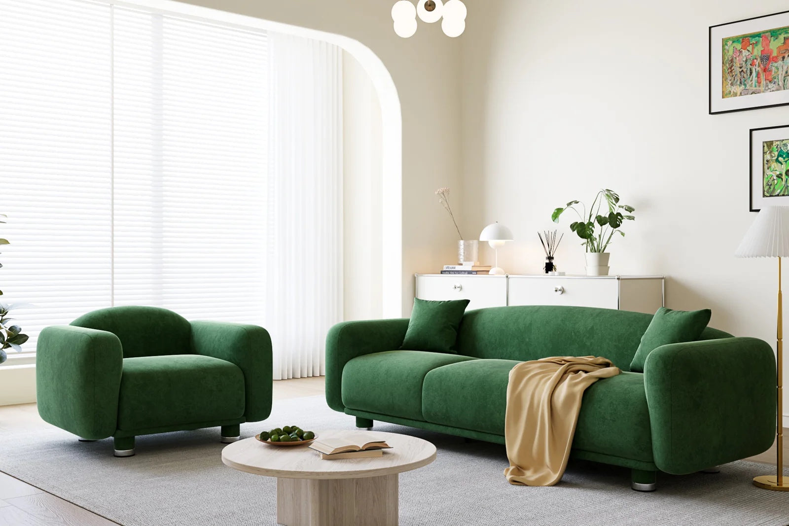 An evergreen sofa with a yellow blanket draped over and a matching armchair in a white living room with a round coffee table. 