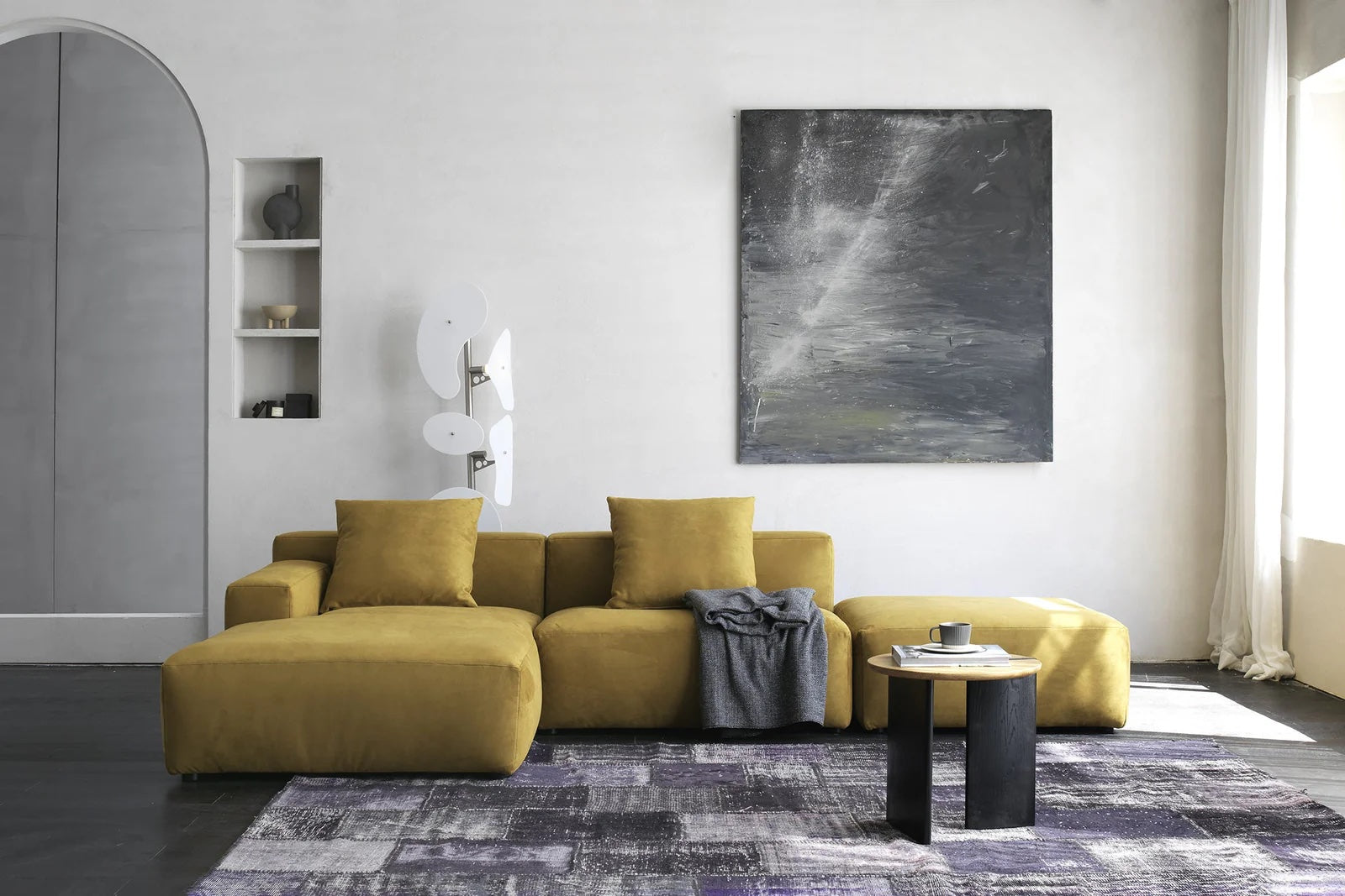 Yellow sectional sofa on top of an abstract rug with a small table in front of it. 