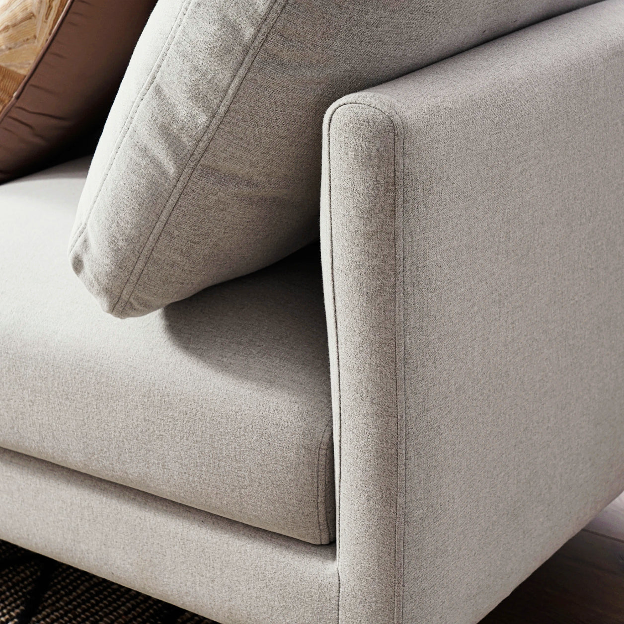 Close-up of the Adams Chaise Sectional Sofa's armrest by Castlery, showcasing its light gray fabric upholstery. The angled armrest is paired with a matching cushion, highlighting its sleek modern design aesthetic through clean lines and rich texture.