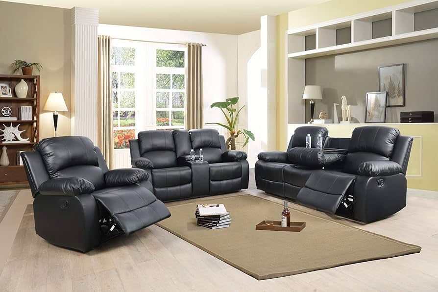A cozy living room with three black leather recliners arranged around a beige rug on a light wood floor. The room is accented with a shelf unit, plants, and large windows bringing in natural light. Books and a glass of water are placed on the rug.
