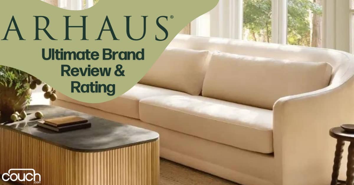 An elegant, cream-colored couch with plush cushions is positioned in a bright, sunny room with large windows. A sleek, modern coffee table with a ribbed base sits in front of the couch. The text reads "ARHAUS Ultimate Brand Review & Rating" in green print.