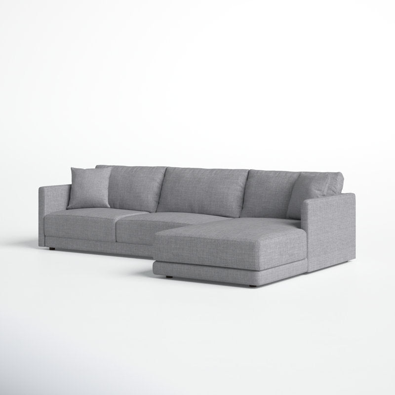 The Astra 2-Piece Upholstered Sectional is a modern gray sectional featuring three seat cushions and a chaise on the right side. It comes with a low backrest and is shown against a plain white background, complemented by two matching pillows placed on the sofa.