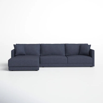 The Astra 2-Piece Upholstered Sectional is a contemporary dark gray L-shaped sofa featuring three seat cushions and a chaise lounge on the left side, set against a plain white wall and floor.