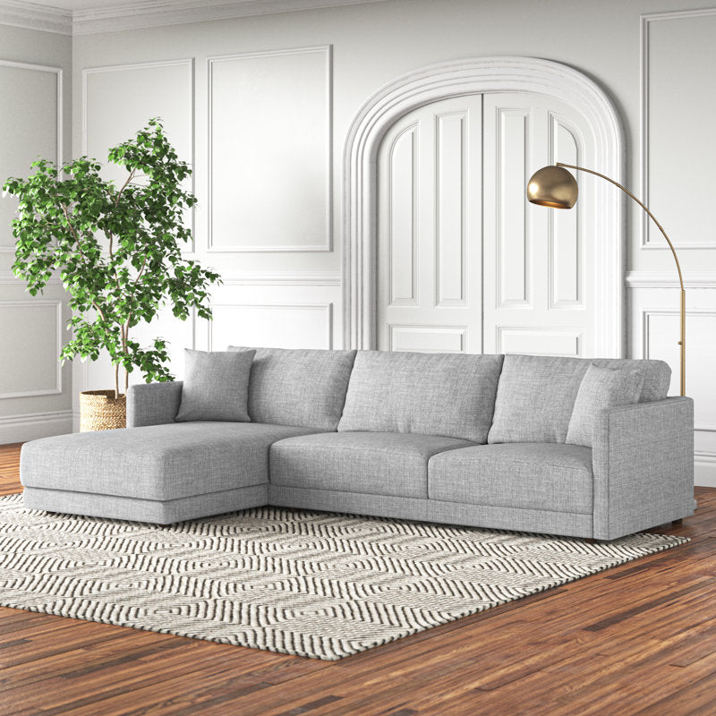 A modern living room featuring the Astra 2-Piece Upholstered Sectional in gray rests on a geometric-patterned rug. A tall gold floor lamp elegantly arches over the sectional. White paneled walls and a large, arched double door create an elegant backdrop, complemented by a leafy green plant on the left.