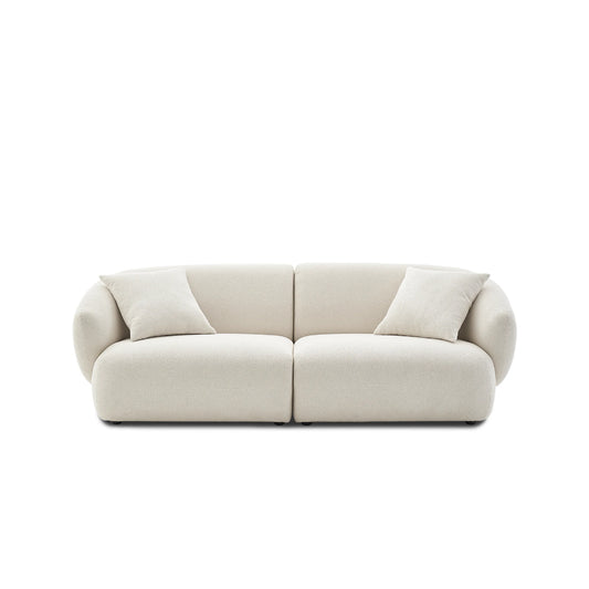 The Auburn Performance Fabric Sofa is a modern, minimalist piece in beige featuring rounded edges and two matching throw pillows, set against a plain white background.