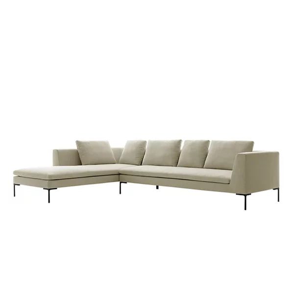 The Charles Left Arm Sectional Sofa by B&B Italia features a light beige, L-shaped design with five cushions. It boasts sleek, modern lines and is supported by thin, black metal legs. The chaise section extends on the left side and is showcased against a white background.