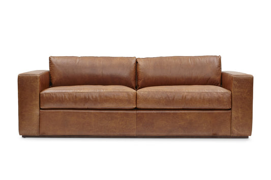 The Bolo Leather Sleeper in Carriage is a boxy, brown leather sofa that includes two large seat cushions and two back cushions. It features wide armrests and boasts a sleek, modern appearance.