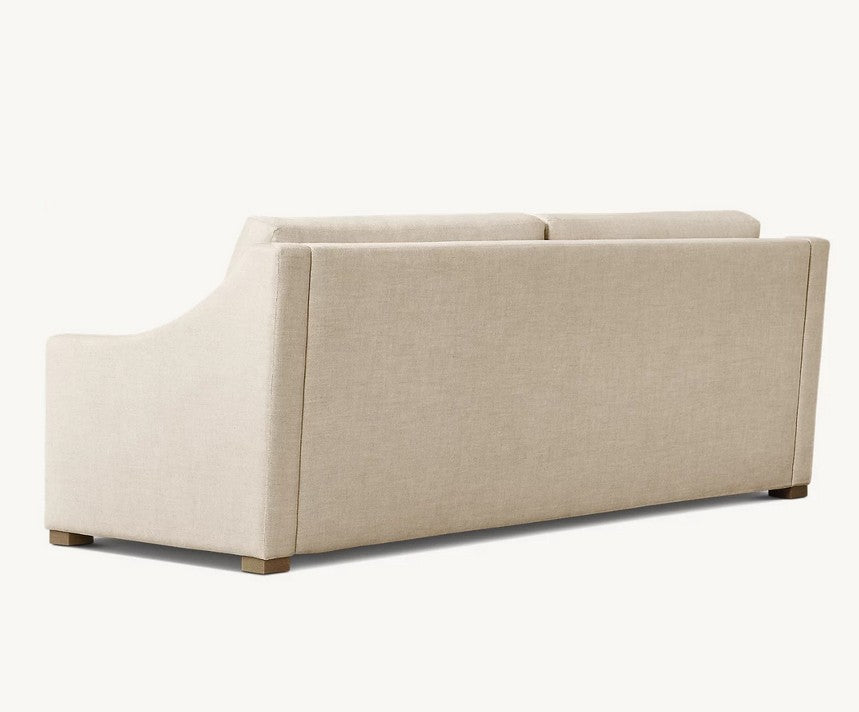 The Belgian Classic Slope Arm Premium Sleeper Sofa, featuring a minimalist design in beige, is shown from the back, highlighting its smooth upholstery and clean lines. The sofa has wooden legs and is set against a plain, light-colored background.