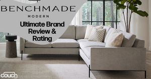 A spacious and modern living room features a light gray sectional sofa with several patterned accent pillows. A small dark side table is positioned beside the sofa holding a plant. Large windows bring in natural light and a leafy plant stands in the corner. Text reads "BENCHMADE MODERN Ultimate Brand Review & Rating.