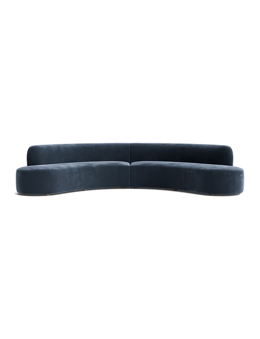 The Cara Sectional Sofa features a curved design in dark blue velvet with no visible legs, set against a black background. It boasts a sleek, minimalist aesthetic with smooth lines and a modern appearance.