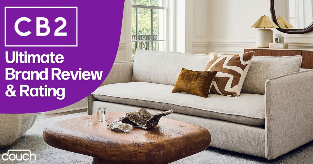 Modern living room with a beige sofa, patterned and solid throw pillows, and a wooden coffee table. Large windows let in natural light. Text on the left reads "CB2 Ultimate Brand Review & Rating.