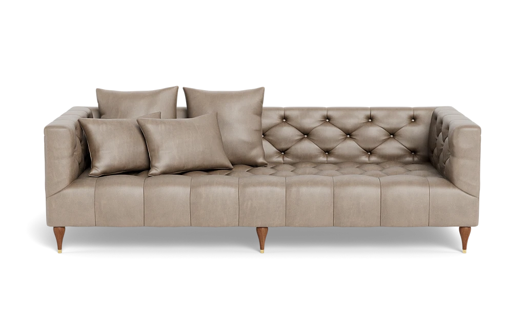 Introducing the Ms. Chesterfield Leather Custom Sofa: a beige, tufted masterpiece in mid-century modern design with wooden legs accented by gold caps. It includes five matching throw pillows and boasts an angular shape with button details for a stylish and elegant appearance.