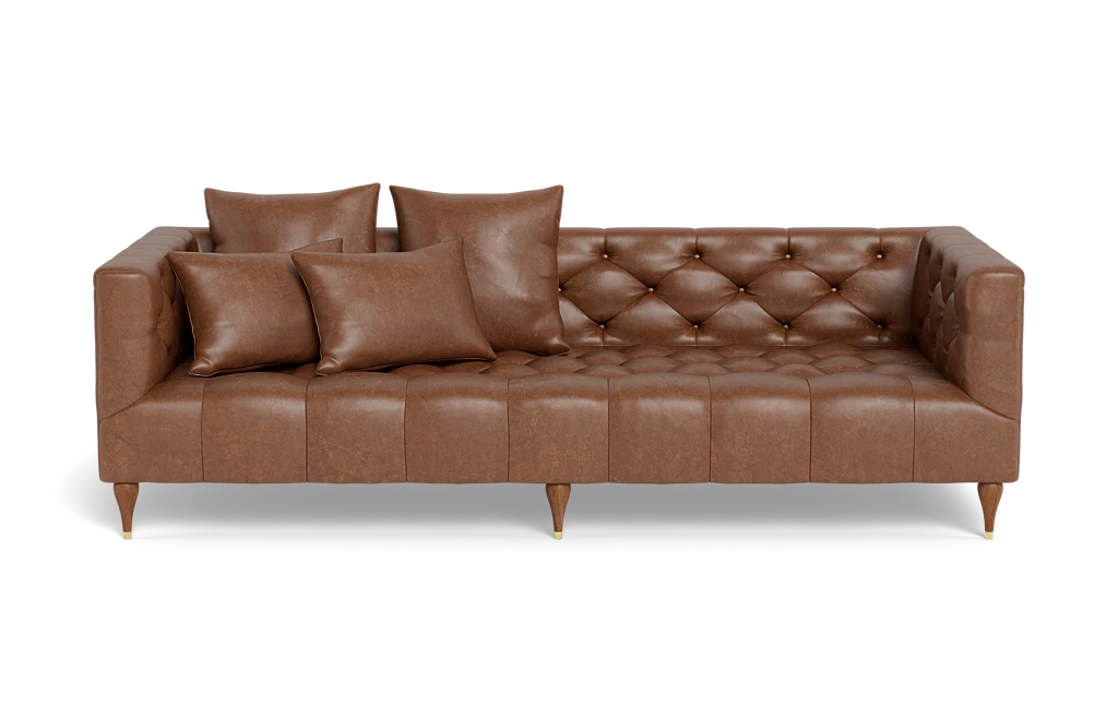 The Ms. Chesterfield Leather Custom Sofa, featuring a classic and elegant design, is upholstered in brown leather with squared arms and back. It stands on wooden legs and is adorned with meticulously arranged matching cushions, including two large and two small ones, enhancing its tufted seating.