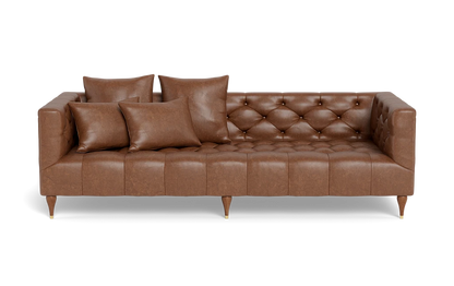 The Ms. Chesterfield Leather Custom Sofa, featuring a classic and elegant design, is upholstered in brown leather with squared arms and back. It stands on wooden legs and is adorned with meticulously arranged matching cushions, including two large and two small ones, enhancing its tufted seating.