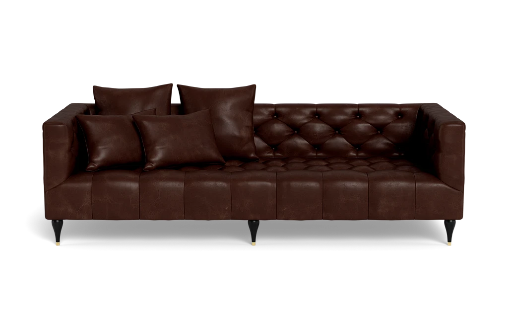 The Ms. Chesterfield Leather Custom Sofa is a dark brown tufted leather piece featuring three seat cushions and four matching throw pillows. It boasts a classic design with black tapered legs and gold tips, set against a black background.