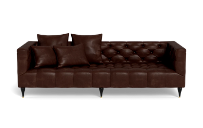 The Ms. Chesterfield Leather Custom Sofa is a dark brown tufted leather piece featuring three seat cushions and four matching throw pillows. It boasts a classic design with black tapered legs and gold tips, set against a black background.