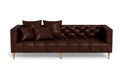 The Ms. Chesterfield Leather Custom Sofa, featuring a luxurious brown leather tufted design and wooden legs, is positioned against a plain background. It is elegantly adorned with four matching cushions, presenting a sleek and modern look.