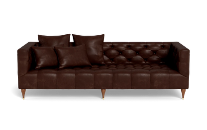 The Ms. Chesterfield Leather Custom Sofa is a dark brown leather piece featuring tufted cushions and paired with four matching pillows. It stands on short wooden legs and is showcased against a plain black background.