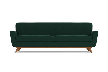 Introducing the Carson Sofa: a dark green, mid-century modern piece featuring a button-tufted backrest and wooden legs. This sofa boasts a sleek, minimalist design complemented by slightly flared armrests.