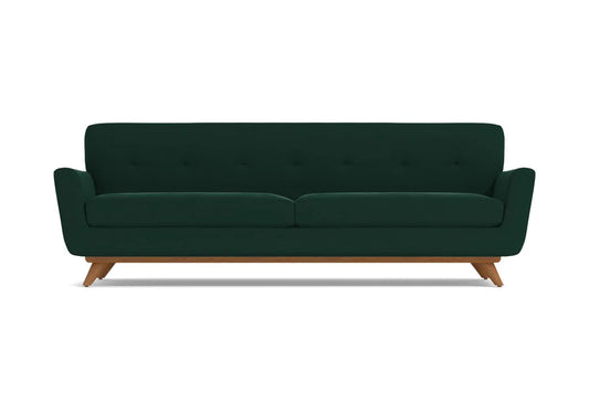 Introducing the Carson Sofa: a dark green, mid-century modern piece featuring a button-tufted backrest and wooden legs. This sofa boasts a sleek, minimalist design complemented by slightly flared armrests.