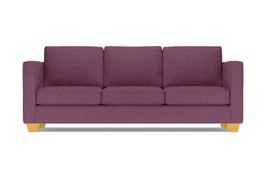 The Catalina Sofa, with its modern design in a purple hue, comes complete with three cushions. It features straight arms and light wooden legs, all showcased against a white background.