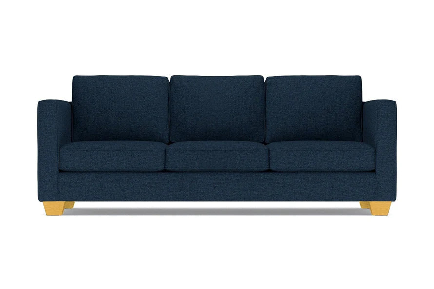 The Catalina Sofa is a dark blue three-seater featuring square cushions and light wooden legs, set against a white background.