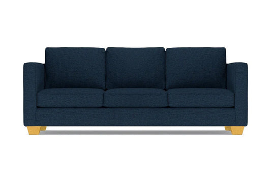 The Catalina Sofa is a dark blue three-seater featuring square cushions and light wooden legs, set against a white background.