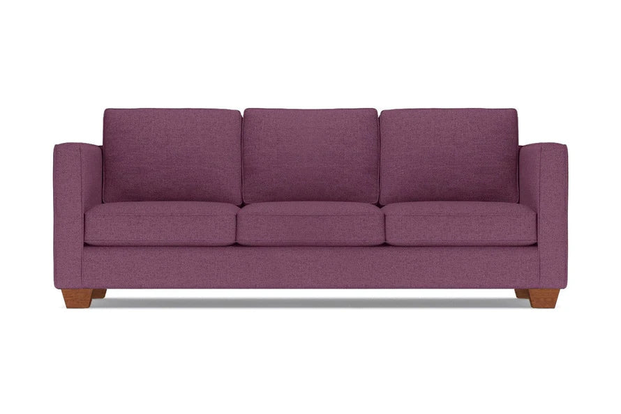 The Catalina Sofa, a plum-colored three-seater with wide armrests and wooden legs, is set against a plain white background. It features three plush seat and back cushions.