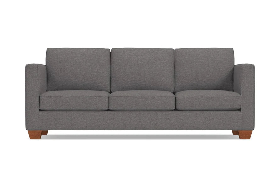 The Catalina Sofa is a gray, three-seater piece with a minimalist design and wooden legs. It features straight arms and three back cushions, set against a plain white background.