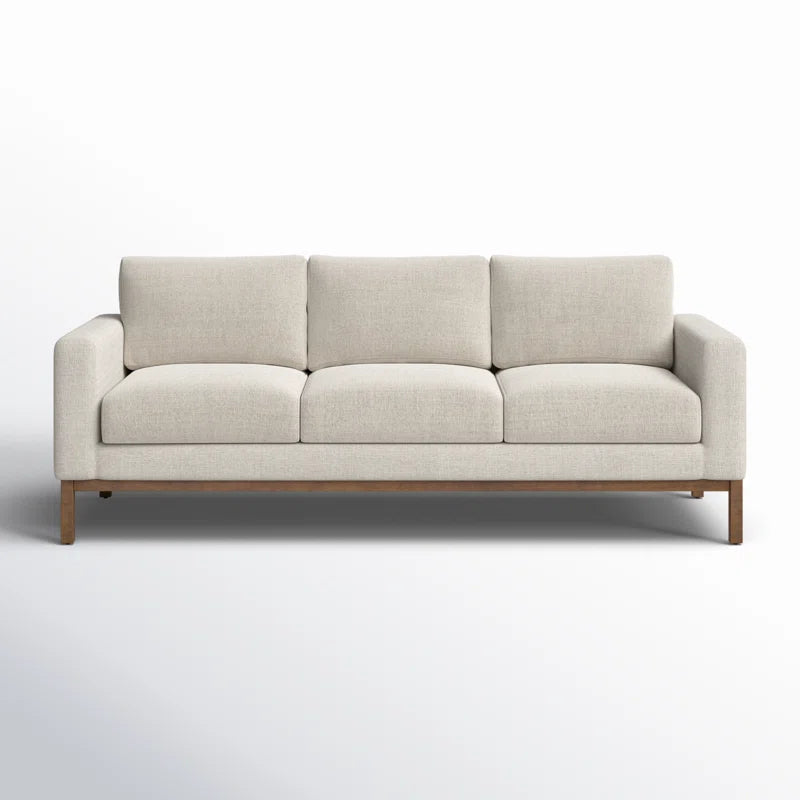 A contemporary Clayton 83.1" Upholstered Sofa in beige, featuring three cushions and a wooden base, set against a neutral backdrop.