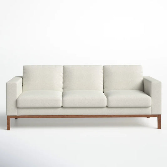 Introducing the Clayton 83.1" Upholstered Sofa, a sleek and modern piece with light beige fabric upholstery. It is designed with three cushions and rests on an elegant wooden base, all set against a plain white background.