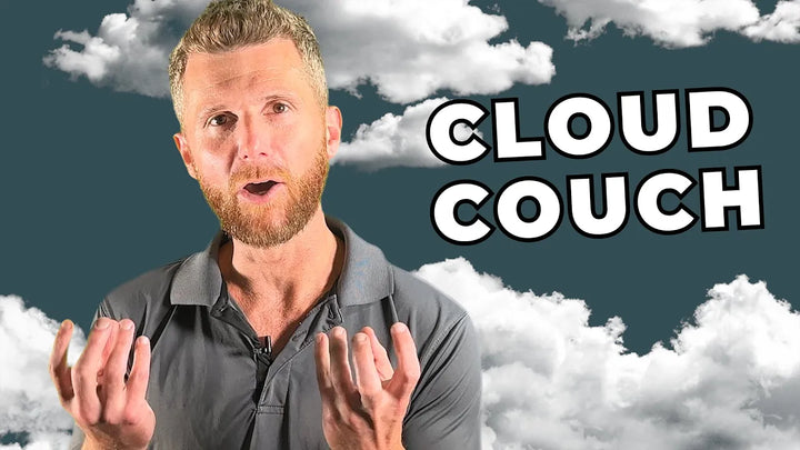 A man with a beard and short hair is speaking with his hands raised. He is wearing a gray polo shirt and standing in front of a backdrop featuring fluffy white clouds. The words "CLOUD COUCH" are written in large, bold letters to his right.