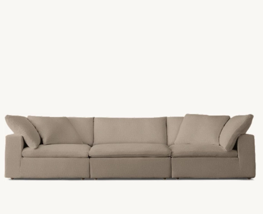 The Cloud Modular 3-Piece Sofa, a spacious and comfortable sectional with plush cushions, is set against a neutral background. It features three sections, including an angled armrest on the left side and a corner piece, offering ample seating space.