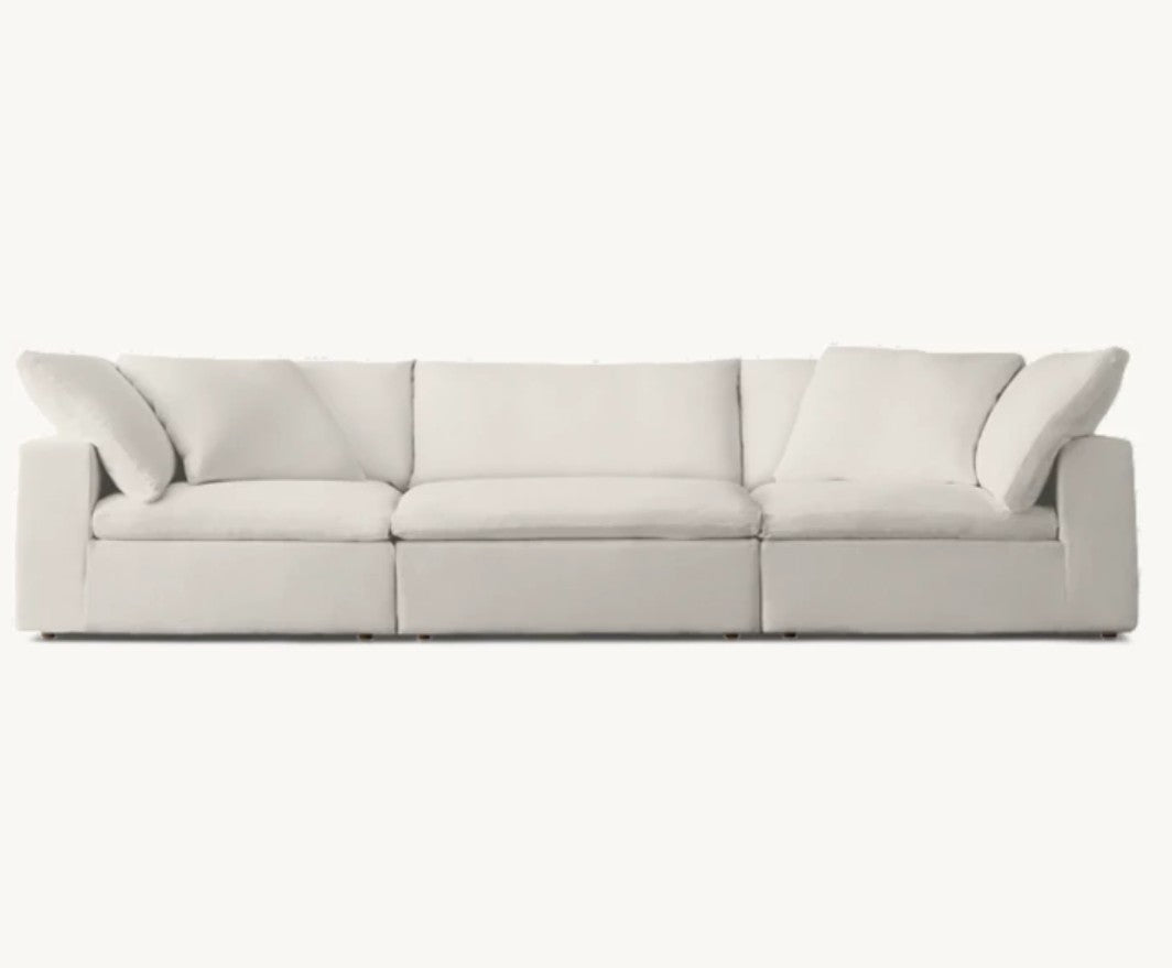 The Cloud Modular 3-Piece Sofa features a modern, minimalist design with a white finish, low armrests, and three cushions. Set against a plain white background, its sleek and spacious construction offers a clean and contemporary look.