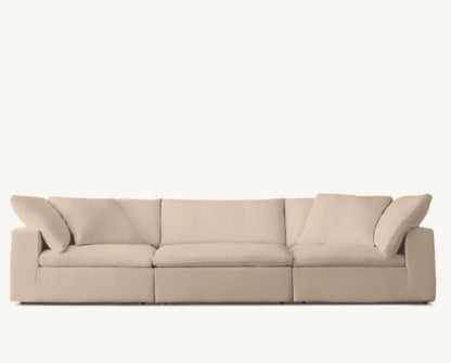 The Cloud Modular 3-Piece Sofa in beige, featuring wide armrests on each end along with three large seat cushions and four back cushions, is set against a solid light-colored background.