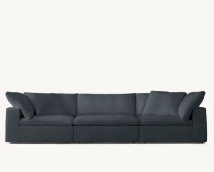 The Cloud Modular 3-Piece Sofa, a spacious three-seater in dark gray with plush cushions, is showcased against a light neutral background. It features wide armrests and boasts a sleek, modern design.