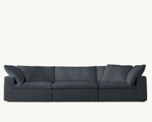 The Cloud Modular 3-Piece Sofa, a spacious three-seater in dark gray with plush cushions, is showcased against a light neutral background. It features wide armrests and boasts a sleek, modern design.