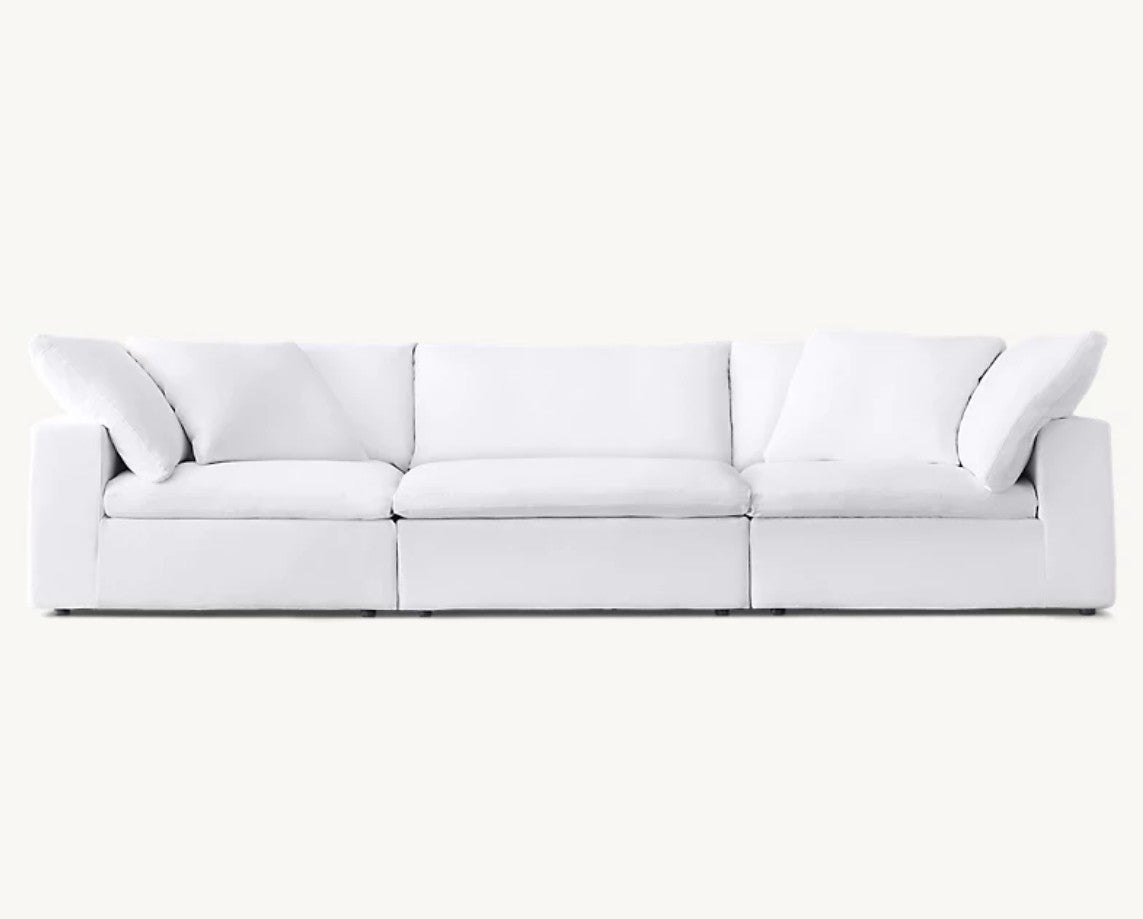 The Cloud Modular 3-Piece Sofa is a modern white sectional featuring plush cushions and an elegant, seamless appearance. Its minimalist design includes rectangular armrests and sits against a plain background.