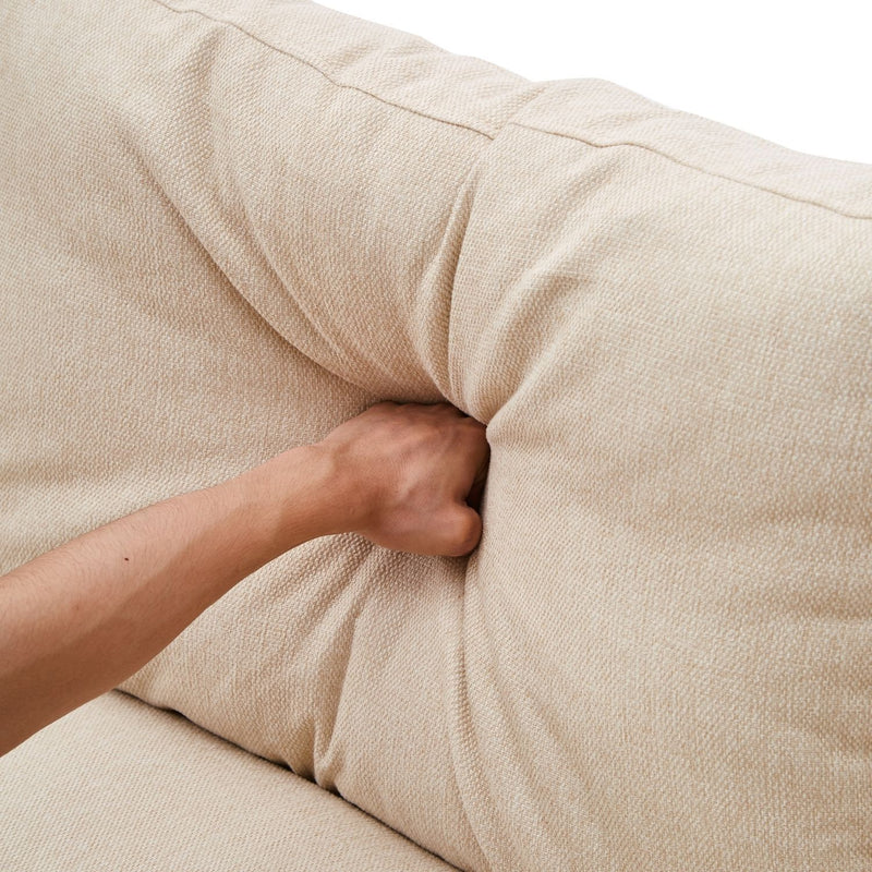 A hand pressing into the cushion of the ValMinimal Sectional in light beige, demonstrating the softness and texture of the fabric.