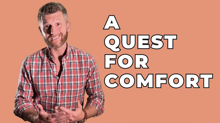 A man in a plaid shirt stands against a peach-colored background, smiling and holding his hands together. To his right, large bold white text reads "A Quest for Comfort.