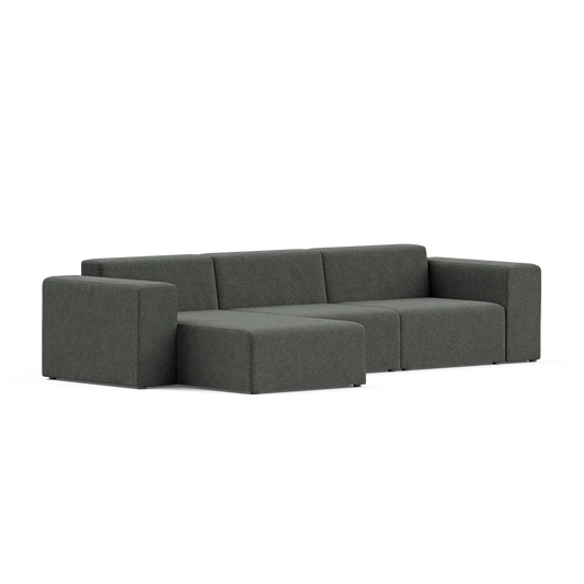 The Three-Seater Form Sectional, featuring a modern dark gray L-shaped design, showcases clean lines with cushioned seats and backrests. Set against a simple backdrop, its minimalistic and contemporary style highlights both comfort and aesthetic appeal.